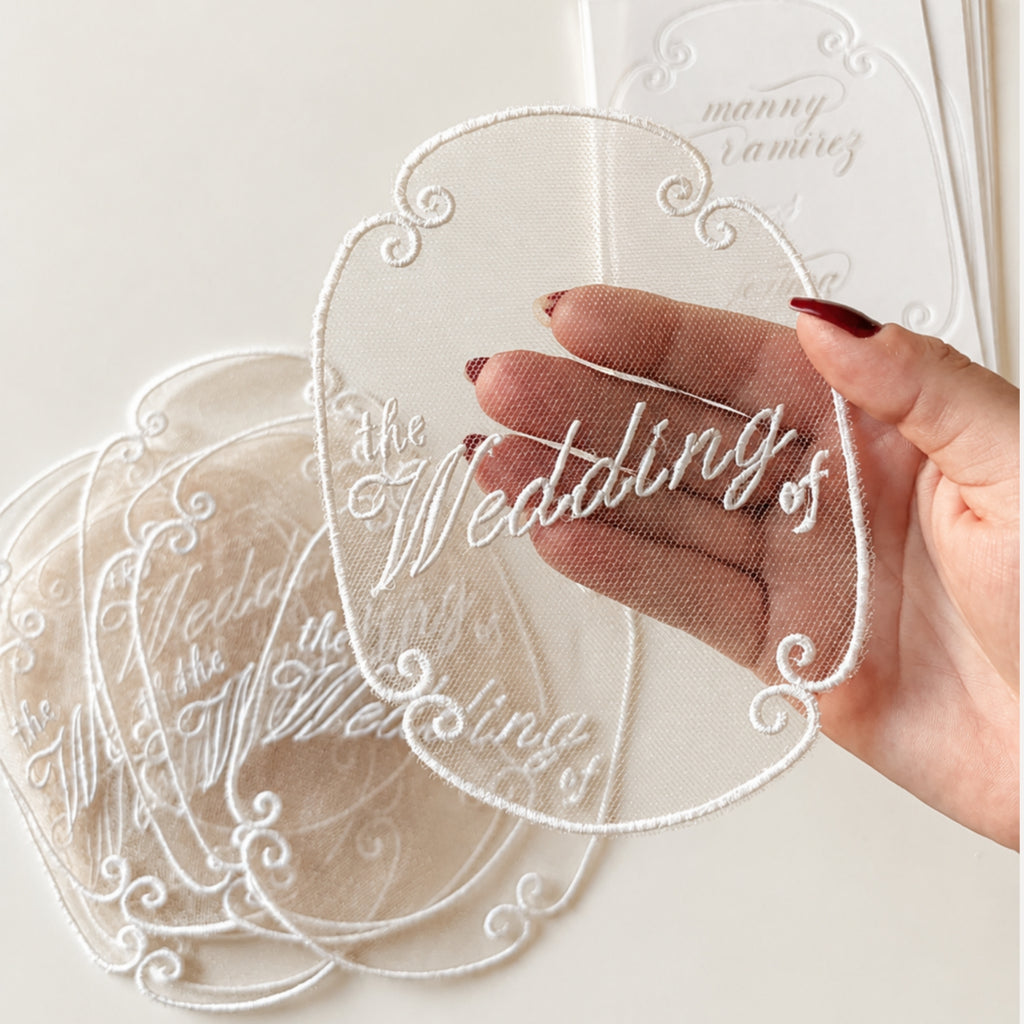Sheer embroidered wedding invitation overlay with white thread lettering and ornate border for custom luxury wedding stationery.